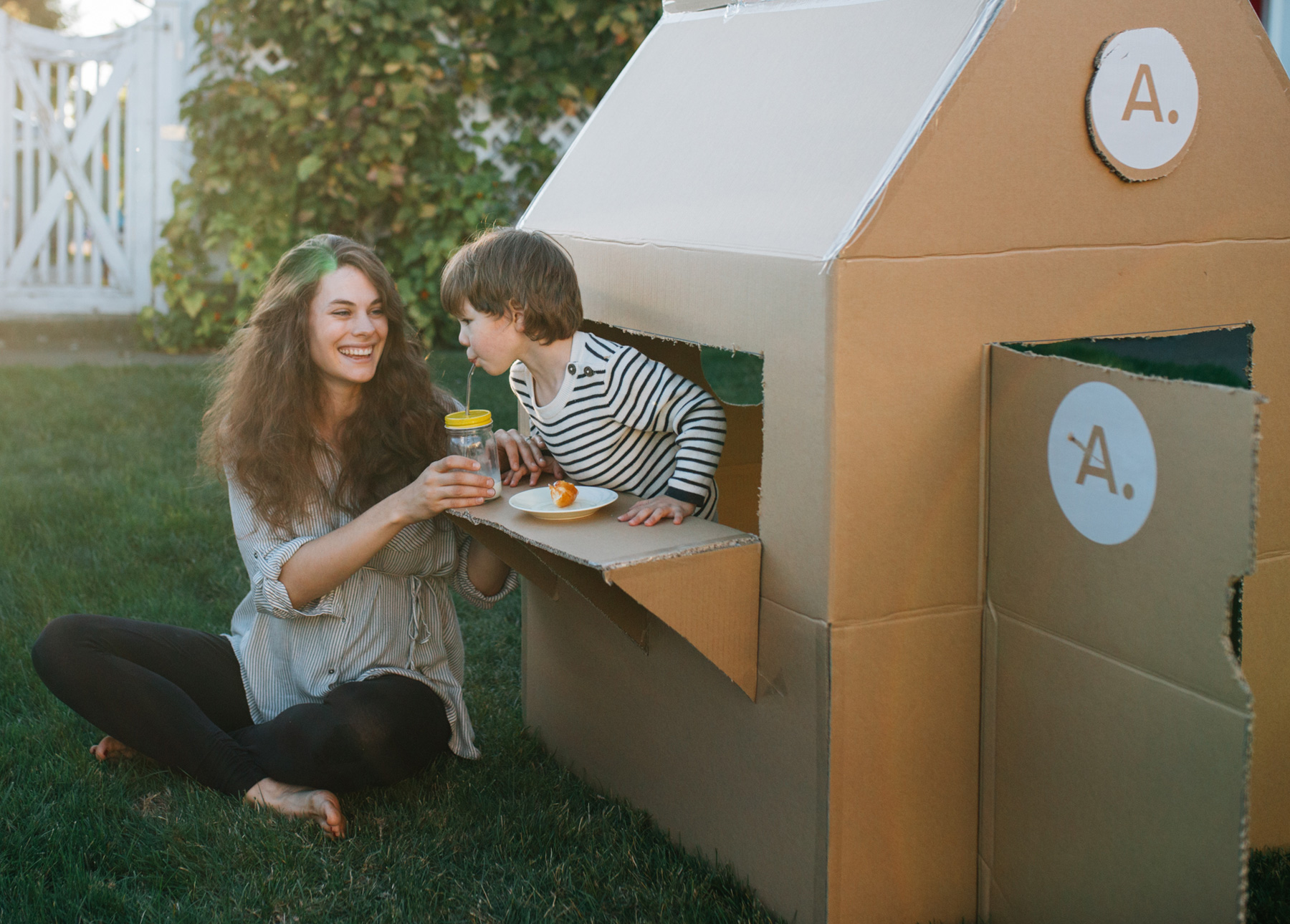 A mother and son enjoy playing with a cardboard box fort.