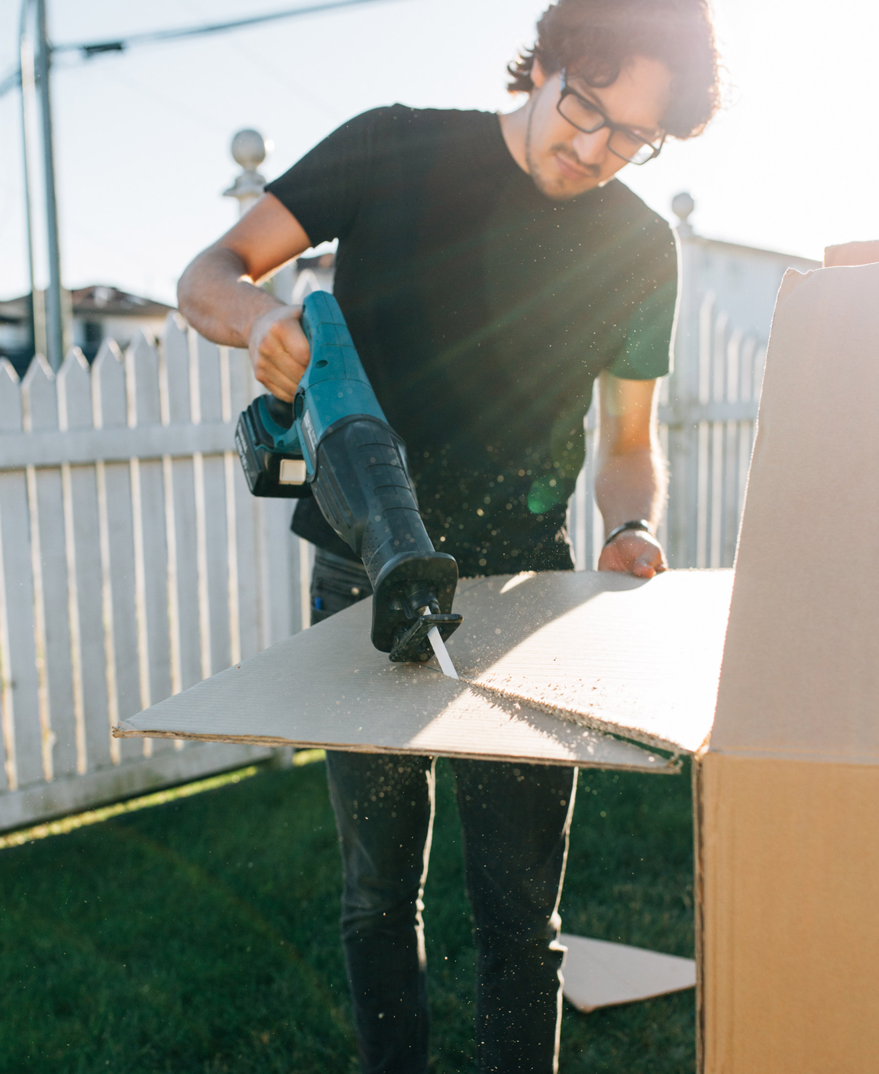Jorge cuts into a cardboard box using a reciprocating saw to create pieces for a box fort.